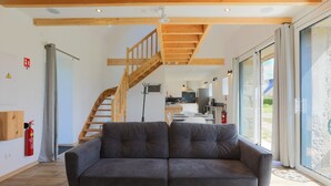 A modern interior with a grey sofa, wooden staircase, and a kitchen in the background. - Holiday Home 'Gite Des Hauts Grève - Near the Sea' with Terrace, Garden & Wi-Fi (Saint-Michel-en-Grève)