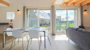 A modern interior with a dining area, a sofa, and large windows. - Holiday Home 'Gite Des Hauts Grève - Near the Sea' with Terrace, Garden & Wi-Fi (Saint-Michel-en-Grève)