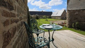 Un bâtiment en pierre doté d’une terrasse en bois, d’une table en métal avec des chaises et d’une cour gazonnée.