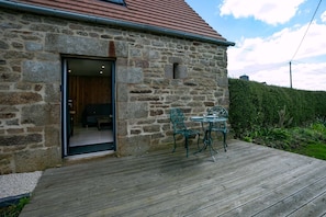 A stone building with a wooden deck, a door leading inside, and two outdoor tables with chairs.
