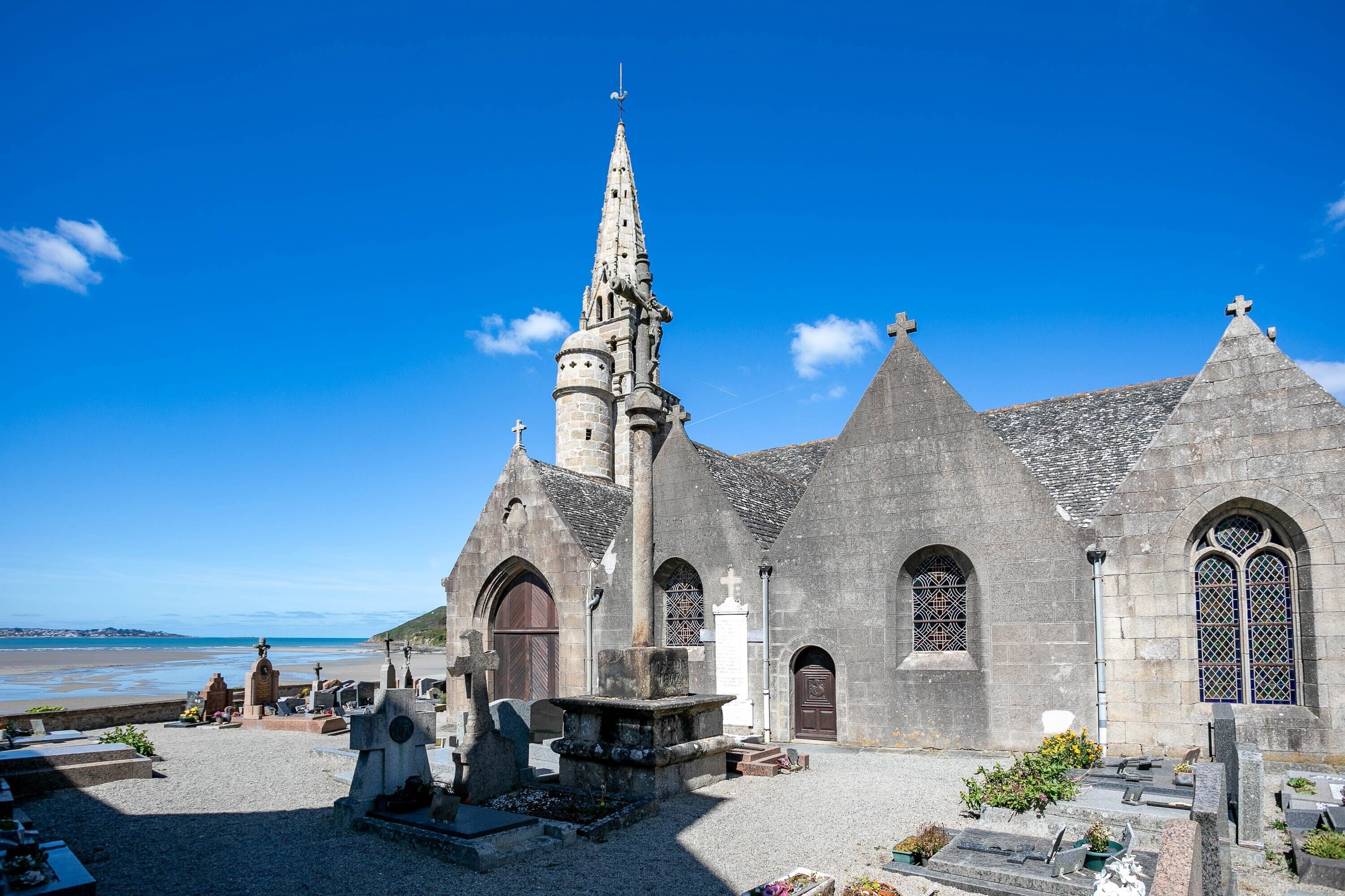 Une église dotée d’un clocher élevé, de fenêtres en arc et d’un cimetière situé devant.