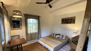 A bedroom with a bed, a desk, a ceiling fan, and a window with curtains. - Secluded Forest Tiny House with Views (Meilhan)