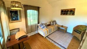 A cozy room with a bed, a wooden table, a chair, and a ceiling fan. - Secluded Forest Tiny House with Views (Meilhan)