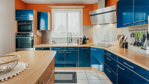 A modern kitchen with blue cabinets, a wooden countertop, and a window with white curtains.