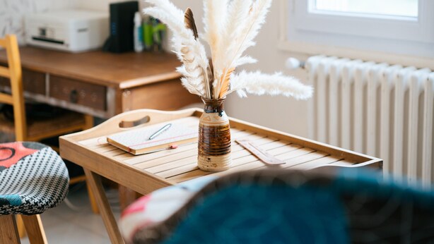 A wooden table with a vase of white feathers, a notebook, and a pen.