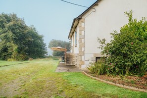 Une maison avec une allée pavée, un espace extérieur aménagé et couvert, et un jardin avec différentes espèces de plantes.