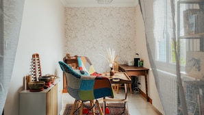 A cozy room with a wooden dining table, a colorful chair, a small cabinet with decorative items, and a window with a view.