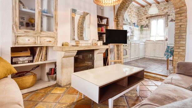 A living room with a fireplace, a television, and a stone archway leading to a kitchen. - Designer Country House Near the Sea (La Nucia)