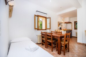 A bedroom with a bed, a wooden dining table with chairs, a kitchen area with a stove, and a window with a view.