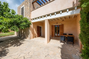A stone patio with a table and chairs, a pergola, and a stone building with shutters.