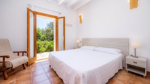 Un dormitorio con cama, mesita de noche, silla y puerta corrediza que da a un balcón.