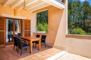 A patio with a wooden table and chairs, a hanging light fixture, and a view of trees through a window.