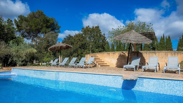 Una piscina con agua azul con azulejos, rodeada de sillas de descanso y un paraguas de paja.