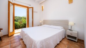 Ein Schlafzimmer mit Bett, Nachttisch und Blick auf Grün durch eine offene Tür.