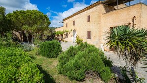 A stone building with a courtyard, surrounded by greenery. - Apartment 'Es Sestador' with Mountain Views, Shared Pool and Wi-Fi (Illes Balears)