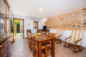 A dining area with a wooden table, chairs, and a stone wall. - Apartment 'Sa Boal' with Mountain Views, Shared Pool and Wi-Fi (Illes Balears)