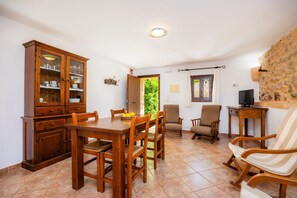 Un comedor con una mesa de madera, sillas, un armario con puertas de vidrio y un televisor sobre un mueble de madera.
