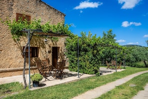 Un edificio de piedra con una pérgola, mesas al aire libre y un sendero.