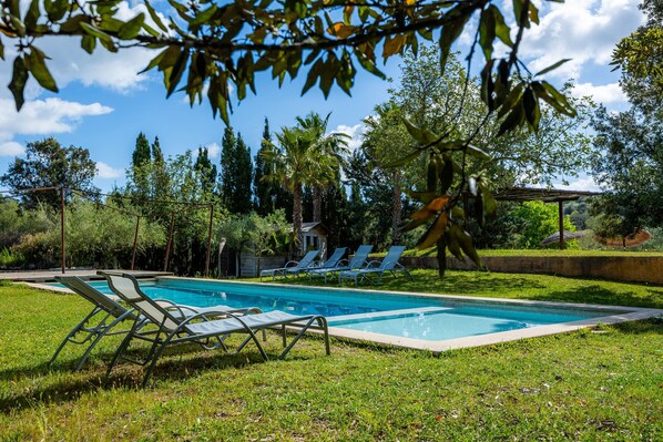 A swimming pool with lounge chairs, surrounded by greenery and trees. - Apartment 'Sa Boal' with Mountain Views, Shared Pool and Wi-Fi (Illes Balears)
