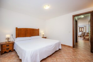 A bedroom with a wooden headboard bed, two bedside tables with lamps, and a tiled floor. - Apartment 'Sa Boal' with Mountain Views, Shared Pool and Wi-Fi (Illes Balears)
