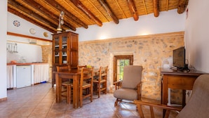 A rustic interior with a stone wall, wooden furniture, a dining area, and a kitchen with white appliances. - Apartment 'Sotil De Ponent' with Mountain Views, Shared Pool and Wi-Fi (Illes Balears)