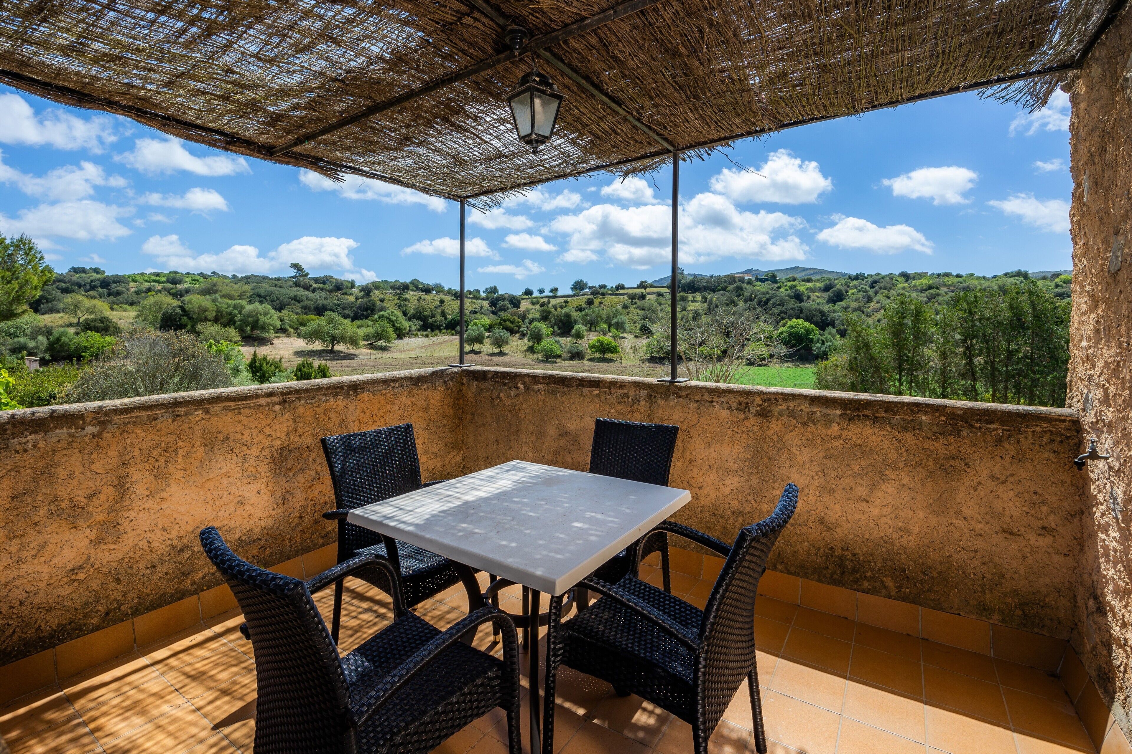 Un área de estar al aire libre techada con mesa y sillas, con vistas a un paisaje montañoso.