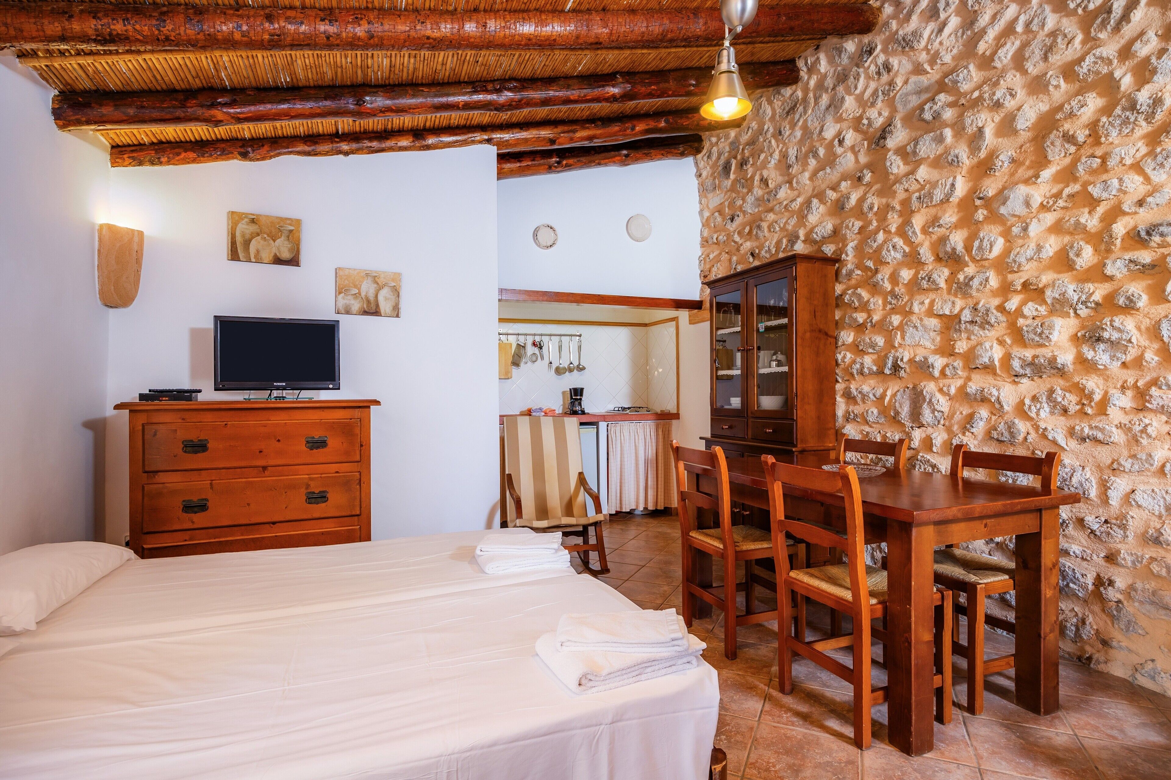 Ein Schlafzimmer mit Bett, Holzkommode, Fernseher und einem Essbereich mit Stühlen und Tisch.
