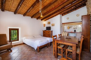 A room with a bed, a wooden dining table, a TV, and a kitchenette.