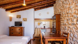 Een kamer met een bed, een houten dressoir, een televisie, een eettafel met stoelen, een keukenhoek en een stenen muur.