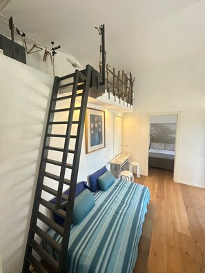 A loft-style bedroom with a bunk bed, a ladder, a desk, and a bed with a striped bedspread.
