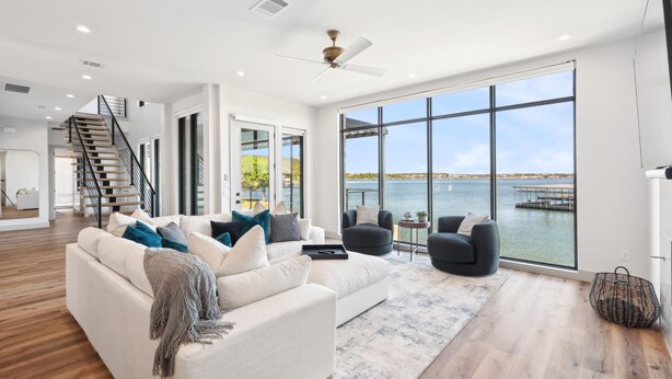 A spacious living room with a large window overlooking a body of water, a staircase, and a modern interior design.
