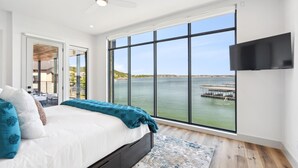 A bedroom with a large window, a bed, a ceiling fan, and a flat-screen TV.