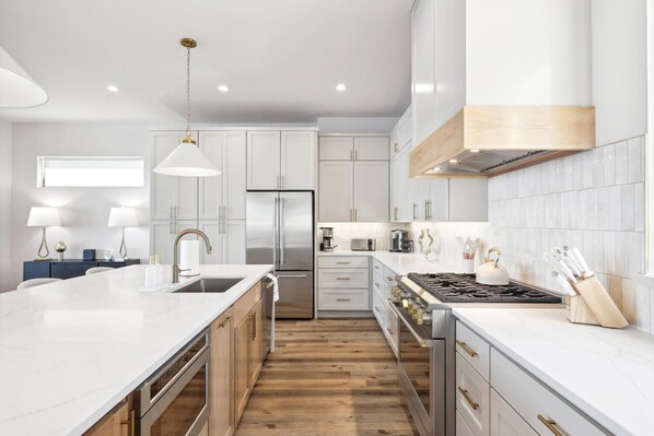 Una cocina moderna con armarios blancos, un refrigerador de acero inoxidable, una estufa a gas y piso de madera.