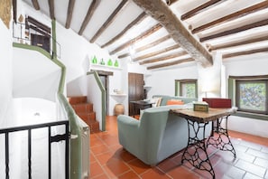 A rustic interior with exposed wooden beams, a staircase, a green sofa, and a table with a radio.