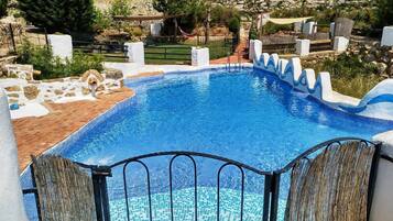 Una piscina con borde de azulejos, rodeada por un muro de piedra y una terraza de madera.