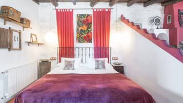 Ein Schlafzimmer mit einem Bett, roten Vorhängen, einem hölzernen Kopfteil, einer roten Wand, einer Treppe und einem Heizkörper.