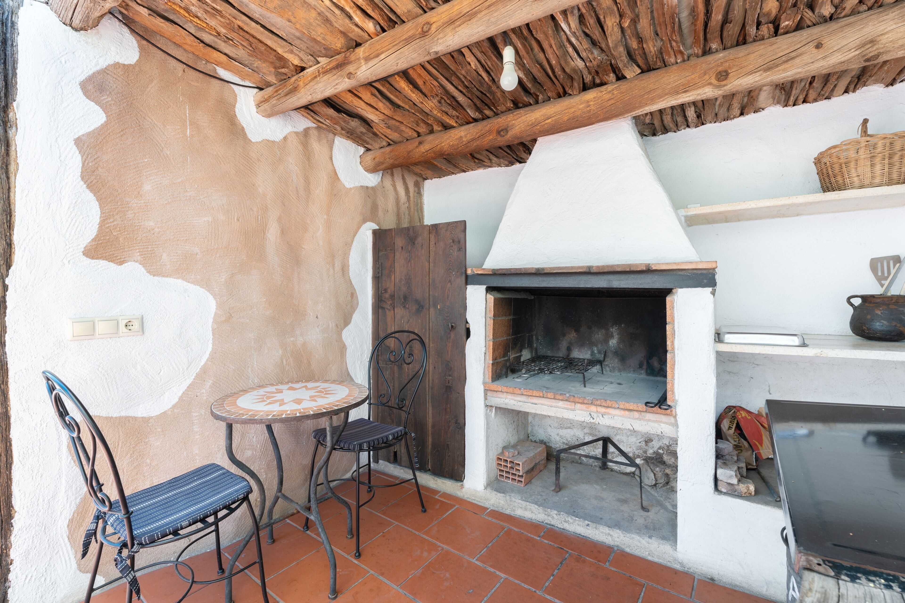 Un espacio al aire libre rústico con una mesa, sillas, una chimenea y un estante con una cesta.