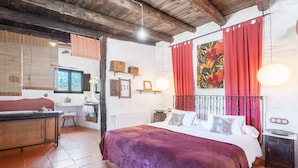 A bedroom with a large bed, a wooden dresser, a small table, a window with blinds, and a red curtain. - Apartment 'Cau' with Mountain Views, Shared Pool and Private Terrace (La Torre D'en Besora)