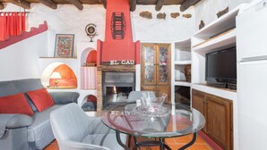 A cozy living room with a fireplace, a glass table, and a sofa with red cushions. - Apartment 'Cau' with Mountain Views, Shared Pool and Private Terrace (La Torre D'en Besora)