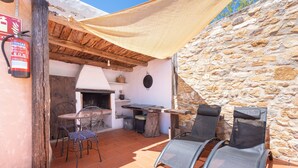 An outdoor patio with a stone wall, a fire extinguisher, a table, chairs, and a grill. - Apartment 'Cau' with Mountain Views, Shared Pool and Private Terrace (La Torre D'en Besora)