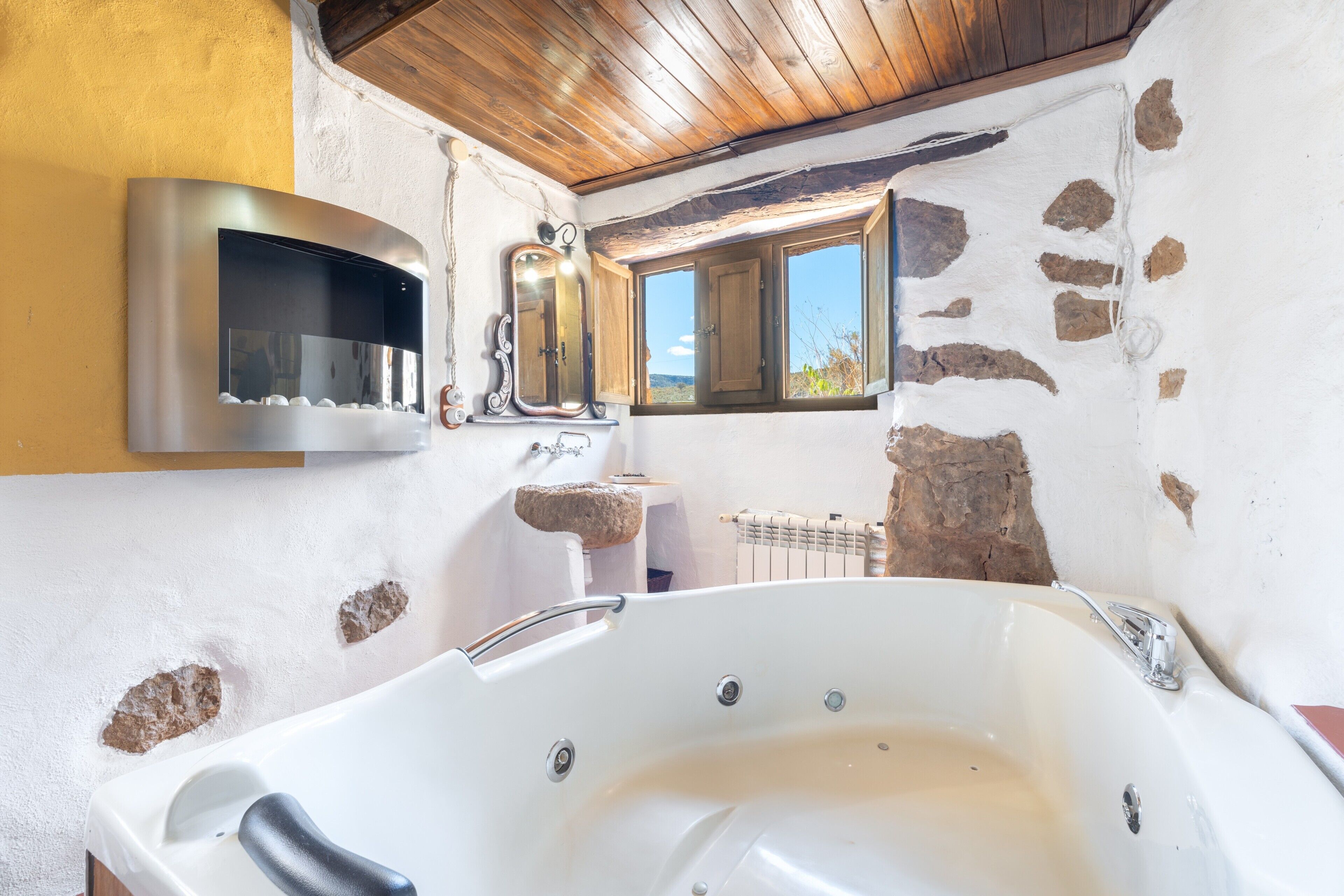 Ein Badezimmer mit einer großen Badewanne, einem Spiegel, einem Steinsink und einem Fenster mit Blick.