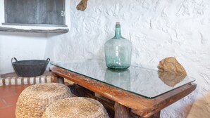 Um interior rústico com uma mesa de vidro, cestos de palha, um balde de metal e uma parede de pedra.