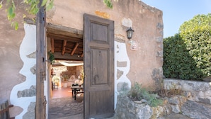 Uma porta de madeira aberta que dá para um quarto com soalho de pedra, decoração rústica e parede de pedra com uma pequena janela.