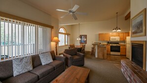 Ein großzügiges Wohnzimmer mit Sofa, Couchtisch und Kamin. Es gibt eine Küchenzeile mit Holzschränken und einem Esstisch.