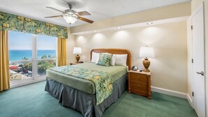 Een hotelkamer met een bed, twee nachtkastjes, een plafondventilator en uitzicht op de oceaan.