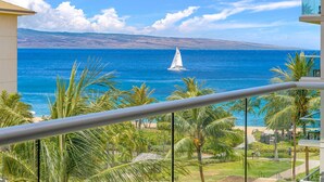 A balcony with a view of the ocean, palm trees, and a distant sailboat.