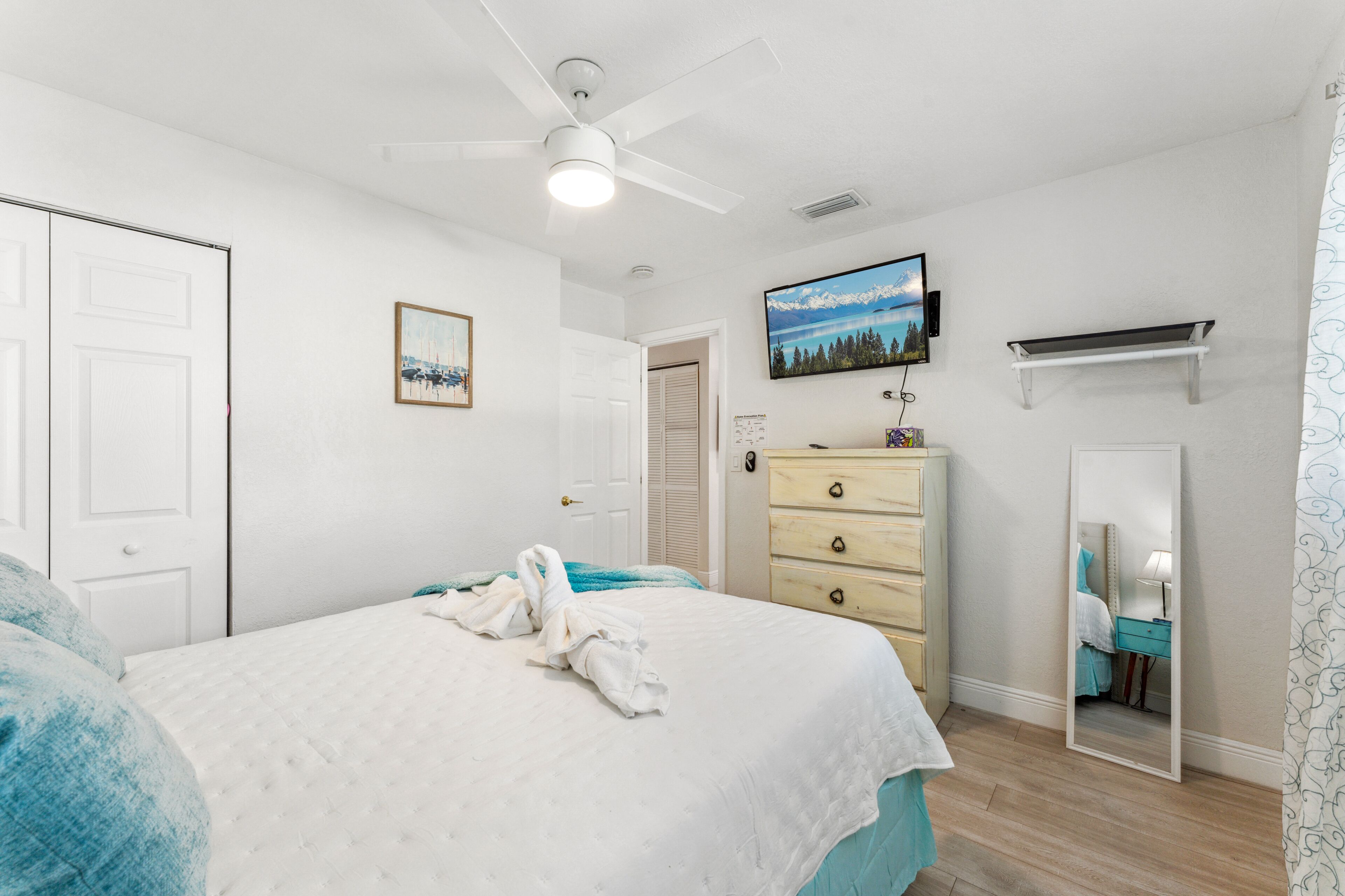 A bedroom with a bed, a dresser, a television, and a mirror.
