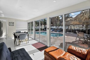 A modern living room with a glass door leading to a pool area, a dining table, and a leather sofa.