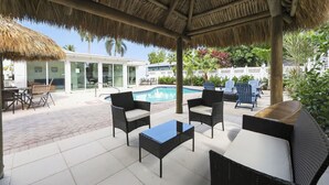 Un espacio al aire libre techado con mobiliario de mimbre, una piscina y vistas a una casa.
