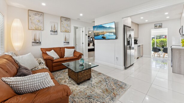 Un salón moderno con un sofá de cuero marrón, una mesa de centro de cristal y un televisor de pantalla plana grande montado en la pared.